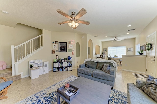 living area featuring ceiling fan, visible vents, arched walkways, light tile patterned floors, and stairs
