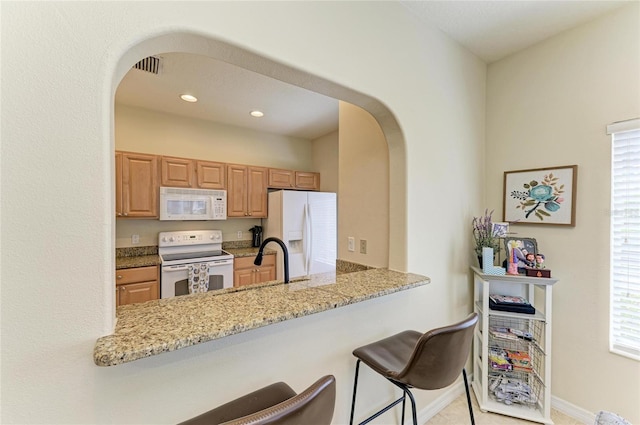 kitchen with a peninsula, white appliances, a kitchen bar, light stone counters, and arched walkways