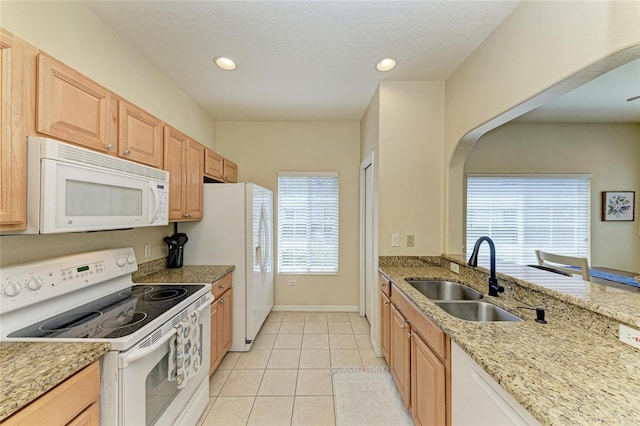 kitchen with a sink, light tile patterned floors, baseboards, light stone counters, and white appliances