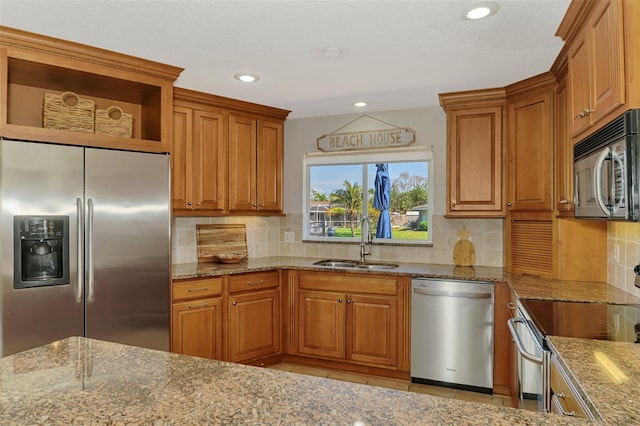 kitchen with stainless steel appliances, open shelves, a sink, and light stone countertops