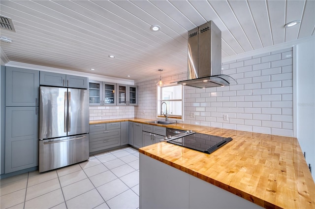 kitchen with glass insert cabinets, butcher block countertops, island range hood, a sink, and appliances with stainless steel finishes