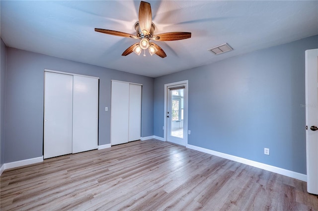 unfurnished bedroom featuring visible vents, baseboards, two closets, and wood finished floors