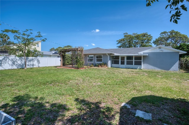 rear view of house with fence, a shingled roof, stucco siding, a sunroom, and a yard
