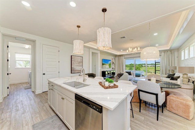 kitchen featuring stainless steel dishwasher, a center island with sink, a sink, a raised ceiling, and open floor plan