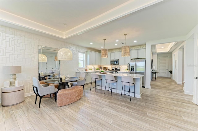 interior space featuring appliances with stainless steel finishes, light wood finished floors, a raised ceiling, light countertops, and a kitchen bar