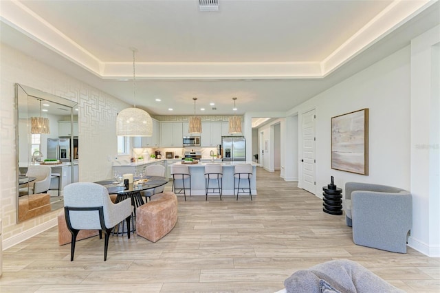 living room featuring recessed lighting, a tray ceiling, baseboards, and light wood-type flooring