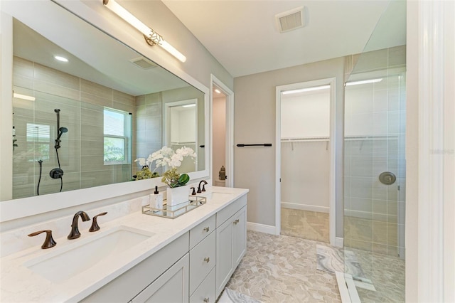 full bath featuring a sink, double vanity, tiled shower, and visible vents