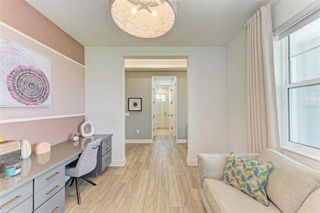 office area with light wood-style floors, baseboards, and built in desk