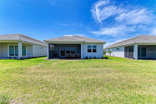 back of house with a lawn, a tiled roof, a sunroom, and stucco siding