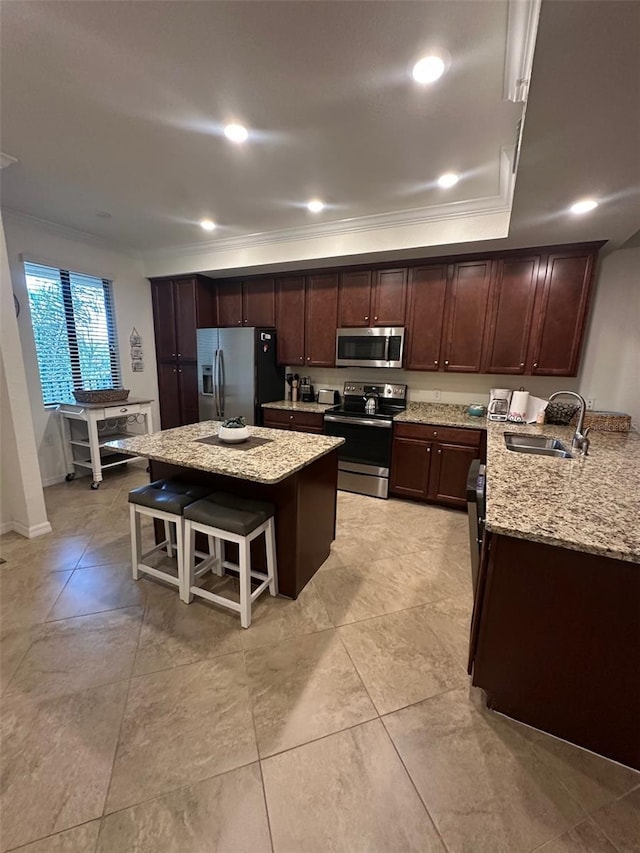 kitchen featuring light stone counters, a sink, a breakfast bar area, a center island, and stainless steel appliances