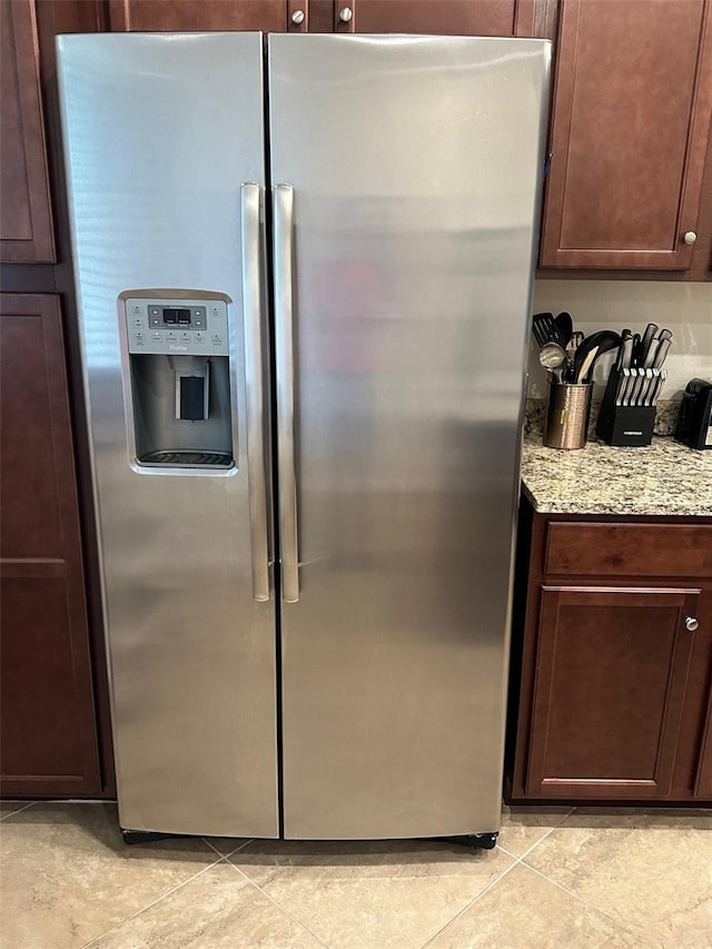 kitchen featuring stainless steel fridge, light tile patterned floors, dark brown cabinets, and light stone countertops
