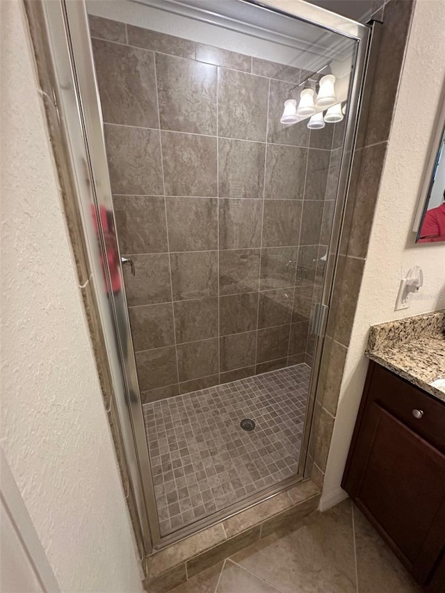 bathroom with tile patterned flooring, a textured wall, a stall shower, and vanity