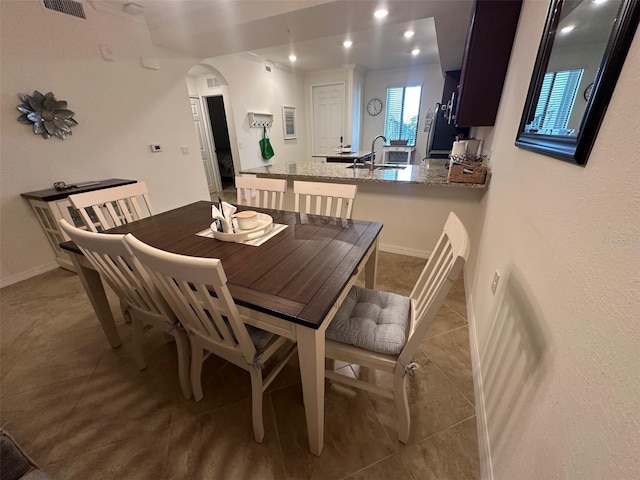 tiled dining space featuring a sink, arched walkways, recessed lighting, baseboards, and visible vents