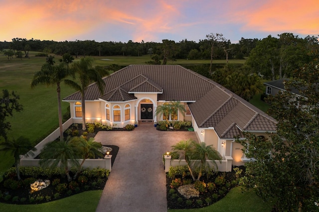 mediterranean / spanish home featuring a tiled roof, curved driveway, and stucco siding