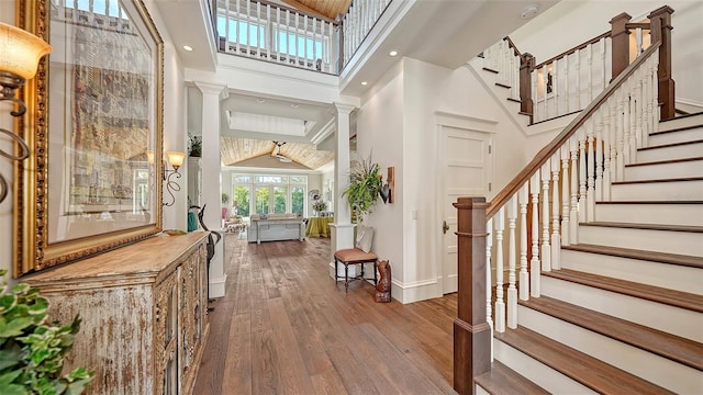 entryway with a high ceiling, decorative columns, baseboards, hardwood / wood-style flooring, and stairs