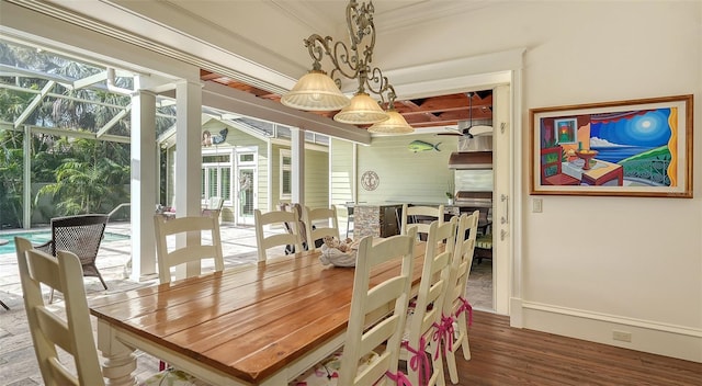 dining room with wood finished floors, ornamental molding, a sunroom, and baseboards