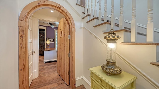hallway with wood finished floors, arched walkways, and baseboards