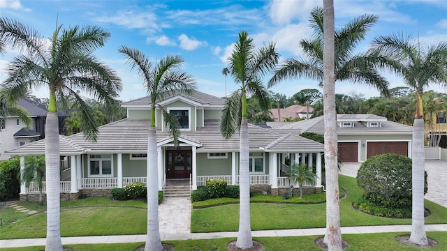 view of front of house with a porch, a tiled roof, a front yard, and a detached garage
