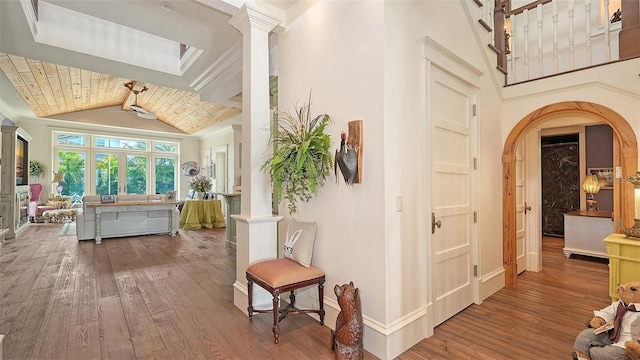 hall featuring hardwood / wood-style floors, decorative columns, arched walkways, baseboards, and beam ceiling