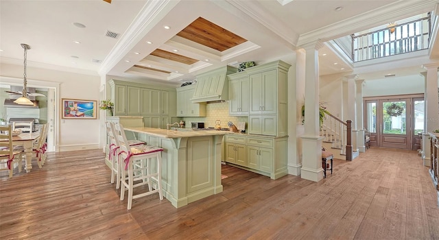 kitchen featuring green cabinets, a breakfast bar, custom exhaust hood, light countertops, and tasteful backsplash