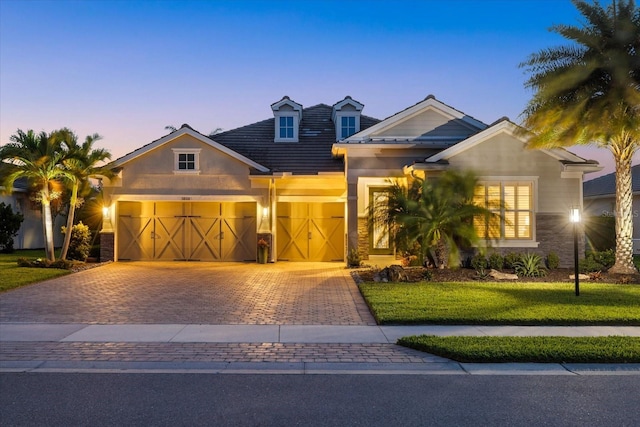 craftsman inspired home featuring decorative driveway, an attached garage, a front yard, and stucco siding