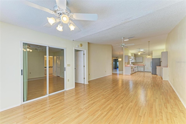 unfurnished living room with a ceiling fan, a textured ceiling, baseboards, and light wood finished floors