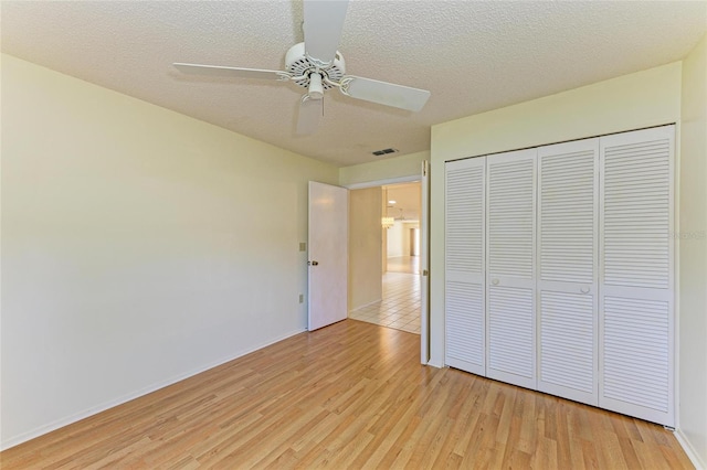 unfurnished bedroom with a textured ceiling, visible vents, baseboards, a closet, and light wood-style floors