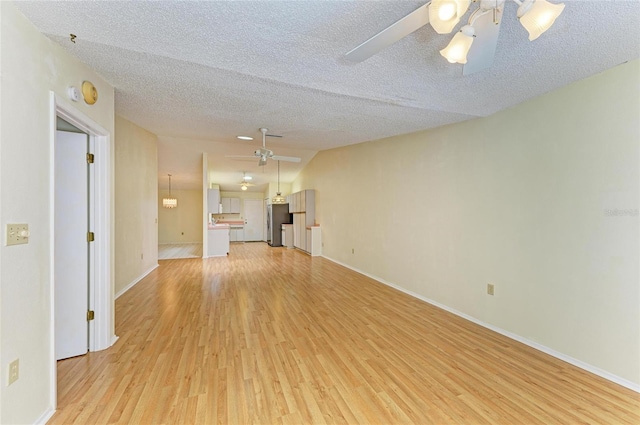 unfurnished living room with baseboards, ceiling fan, light wood finished floors, and a textured ceiling