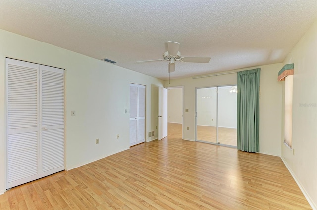 unfurnished bedroom featuring visible vents, a textured ceiling, light wood finished floors, and two closets