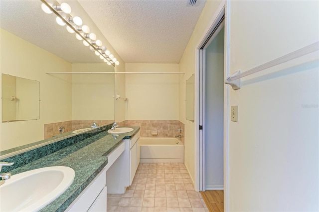 bathroom featuring a textured ceiling, tile patterned flooring, a sink, and a garden tub