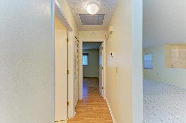 hallway featuring a textured ceiling, baseboards, and visible vents