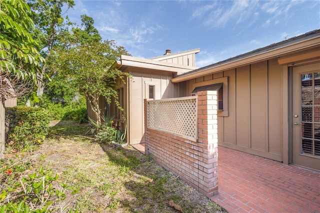 view of side of property with a chimney, board and batten siding, a patio area, and brick siding