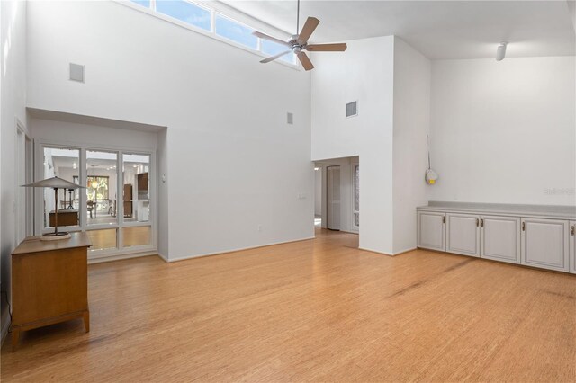 unfurnished living room with light wood-style floors, visible vents, ceiling fan, and a towering ceiling