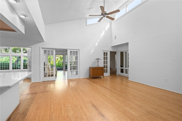 unfurnished living room with french doors, a ceiling fan, a high ceiling, baseboards, and light wood-style floors