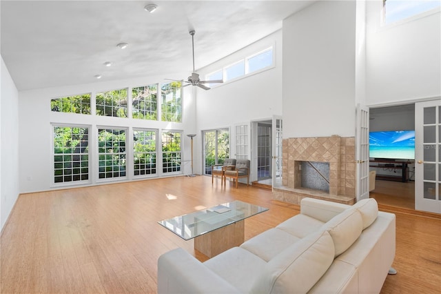 living room featuring a tile fireplace, ceiling fan, a towering ceiling, and wood finished floors