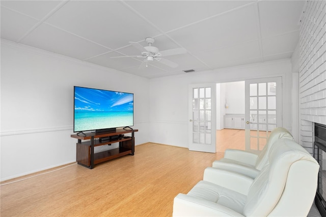 living room featuring visible vents, crown molding, light wood finished floors, a brick fireplace, and ceiling fan