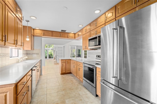 kitchen featuring a sink, a peninsula, decorative backsplash, light countertops, and appliances with stainless steel finishes