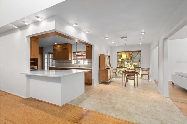 kitchen featuring pendant lighting, brown cabinetry, light countertops, and visible vents