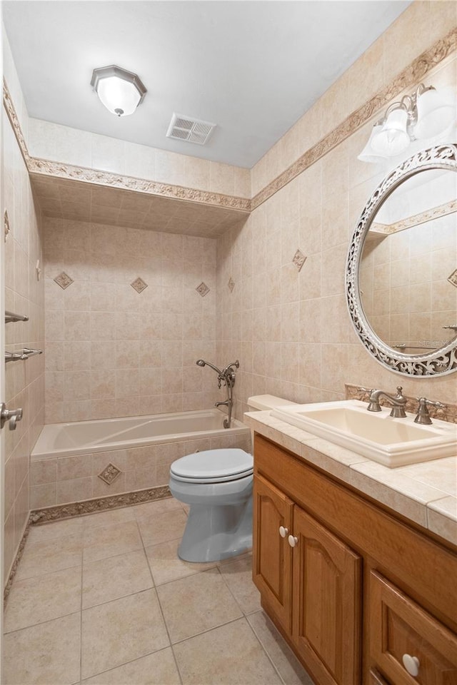 full bath with toilet, a relaxing tiled tub, tile patterned floors, tile walls, and vanity