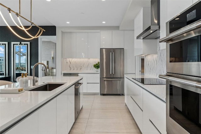 kitchen with appliances with stainless steel finishes, a sink, modern cabinets, white cabinets, and wall chimney range hood