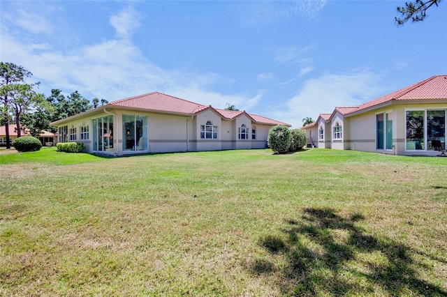 rear view of property featuring a lawn, stucco siding, and a tiled roof
