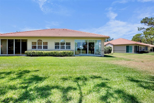 rear view of house with stucco siding, a yard, and a tile roof