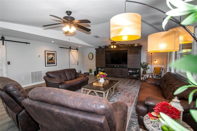 living area with visible vents, a ceiling fan, a barn door, and wood finished floors
