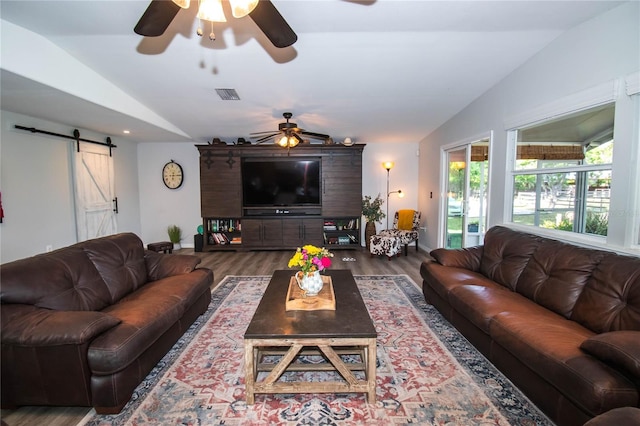 living area with a ceiling fan, lofted ceiling, a barn door, and visible vents