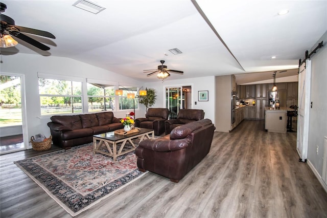 living area featuring visible vents, a ceiling fan, wood finished floors, and a barn door