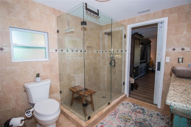 bathroom featuring visible vents, toilet, tile walls, a shower stall, and a sink