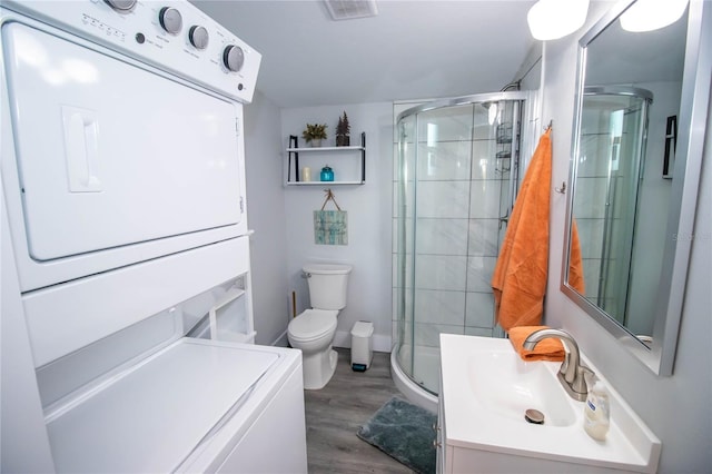 bathroom featuring toilet, wood finished floors, stacked washer / dryer, visible vents, and a stall shower