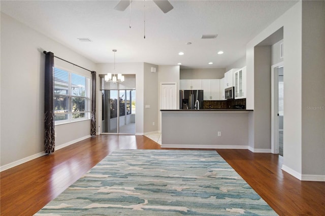 unfurnished living room featuring visible vents, wood finished floors, baseboards, ceiling fan with notable chandelier, and recessed lighting