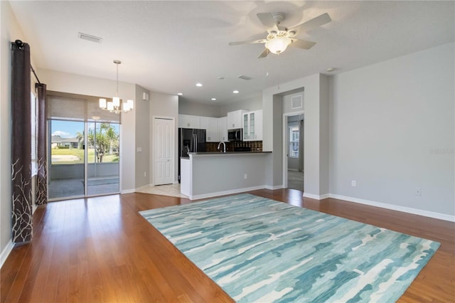 unfurnished living room with visible vents, baseboards, ceiling fan with notable chandelier, and wood finished floors