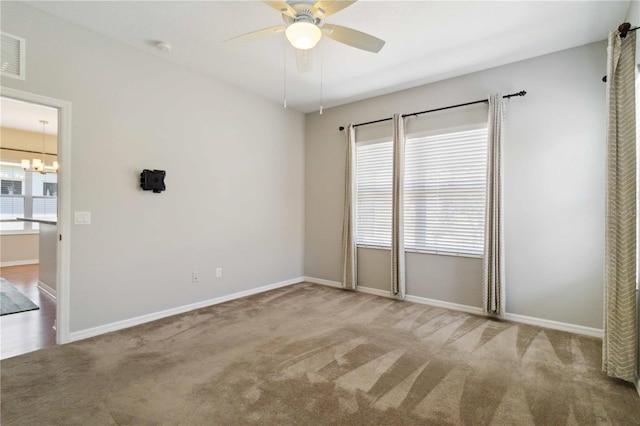 carpeted spare room featuring baseboards, ceiling fan with notable chandelier, and visible vents